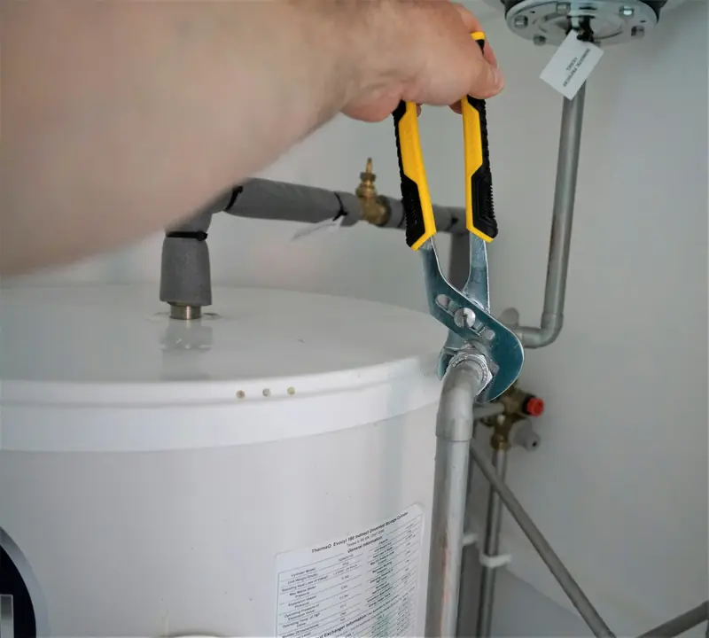 A plumber tightening a fitting on a hot water cylinder